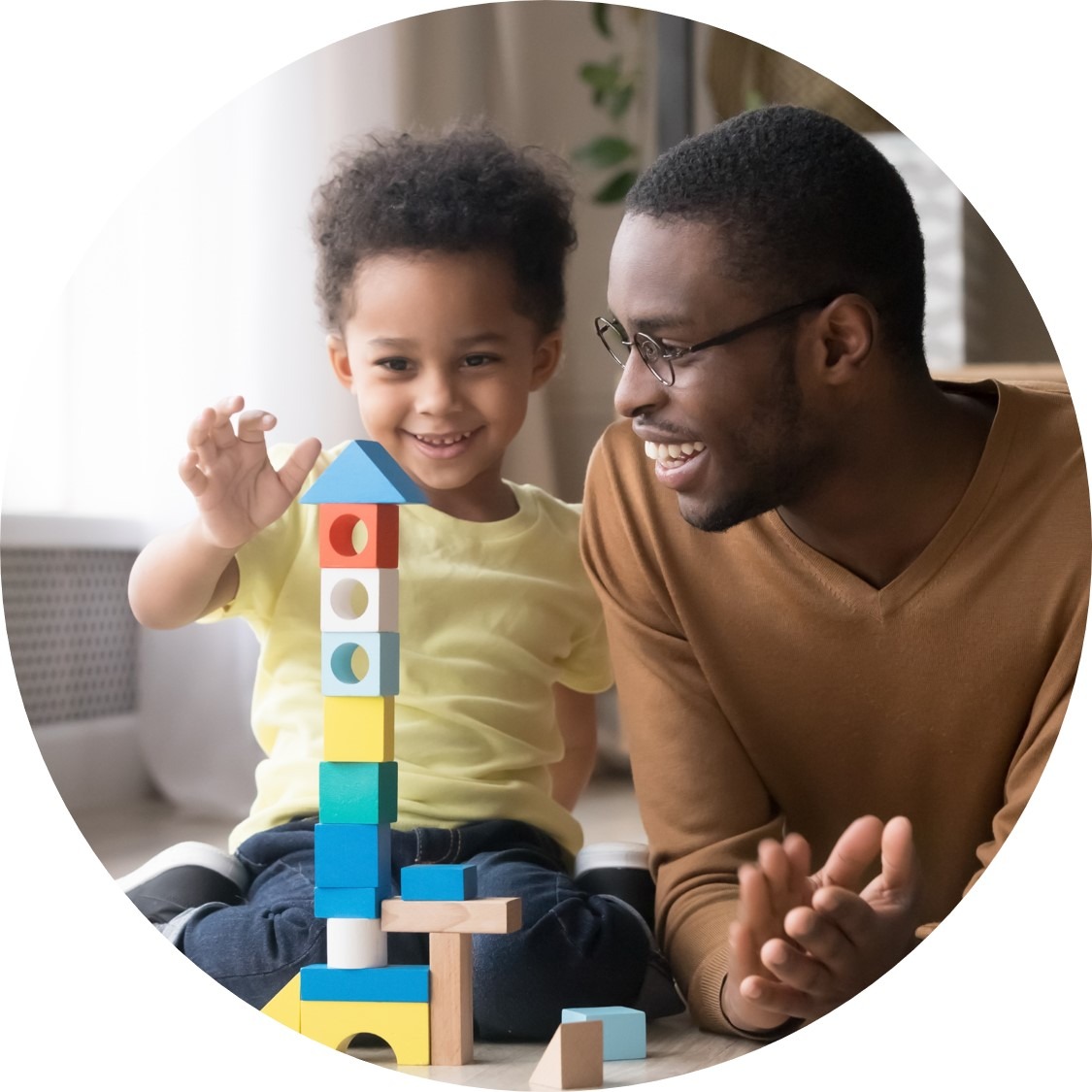 Black man smiles and claps as small Black child plays with blocks