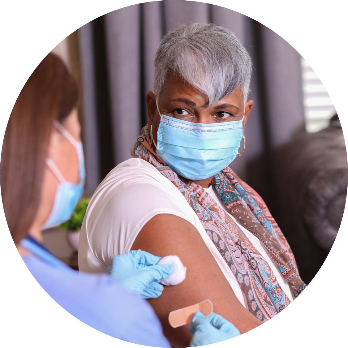 Woman with grey hair and face covering receives bandaid from nurse